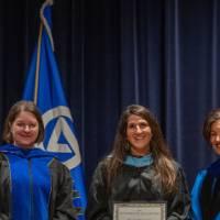 Provost Mili takes picture on stage with 2 faculty and certificates